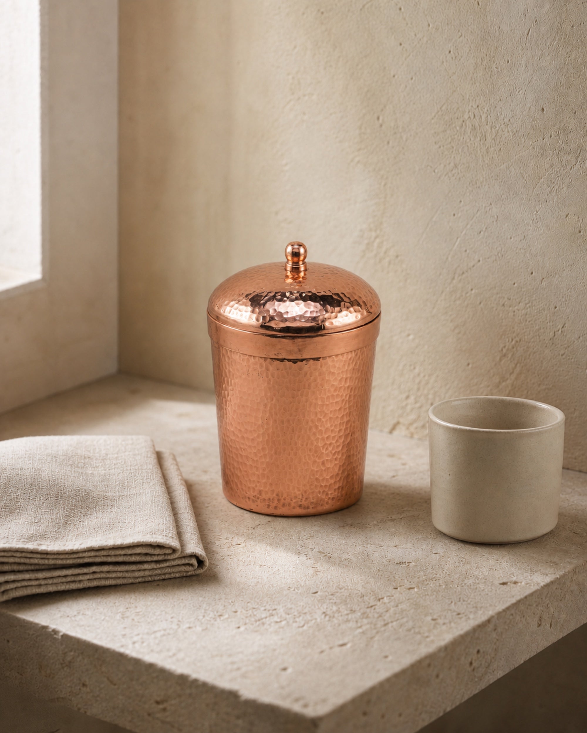 Hand-hammered copper object styled in a quiet warm bathroom